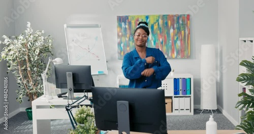 Elegant feisty girl dressed in blue shirt and stylish glasses, dancing in the middle of the office, waving her arms forward, happy for the success of the company, businesswoman with a smile on face