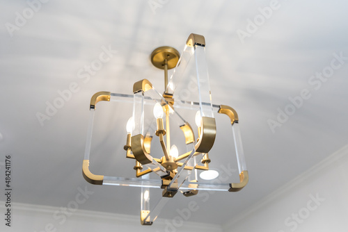 Retro acrylic and glass clear lighting fixture with warm brushed gold accents against a white wall