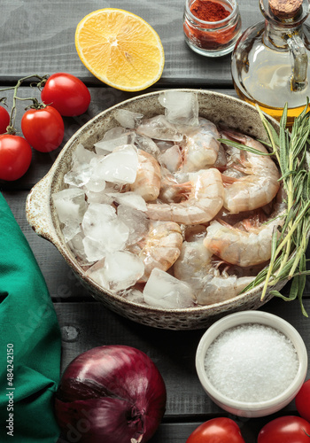 Fresh king, wannamei prawns in a plate with lemon, rosemary, tomato and crushed ice, top view. selective focus