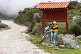Women sitting on a rock next to a bus stop at a sandy path in the mountain