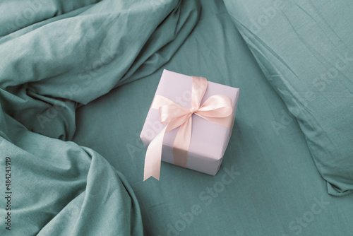 Purple gift box present with pink bow on a grey bed in morning in bedroom. Christmas, New Year, Valentine's Day and birthday concept