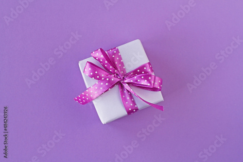 Gift box with white polka dot ribbon bow on purple background © yulyao
