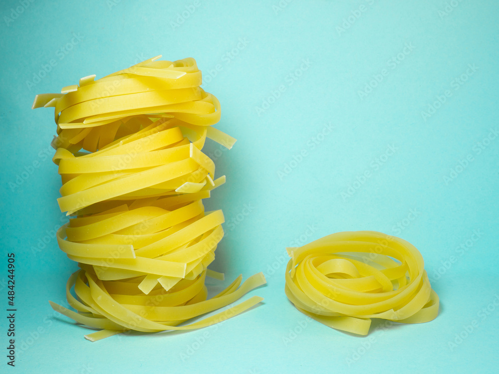 Nests of pasta on a blue background. Culinary background. Pyramid of noodles. Curled pasta on the table. Uncooked product. Background from noodles. Nests of pasta on a blue background. Culinary background. Pyramid of noodles. Curled pasta on the table. Uncooked product. Background from noodles.