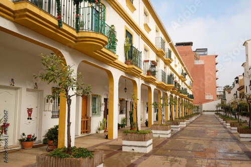 View of residential building with an arch. Apartments with windows, balconies and entrance, typical spanish architecture. Alley with green plants in pots on street. Torremolinos, Andalusia, Spain. photo