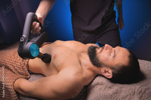 Foto Close-up of a Caucasian male pectoral muscle percussion massager working out in