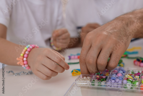 Father with his daughter making beaded jewelry at table, closeup