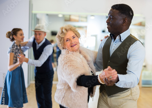 Fotografia Elderly woman learning ballroom dancing in pair in dance studio