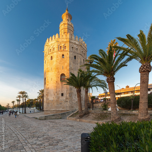 Skyline of Seville with a view on the iconic golden tower on the quayside of the river Guadalquivir on a sunny afternoon, where people enjoy a stroll alongside the water