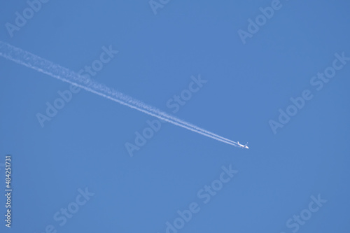 Distant passenger jet plane flying on high altitude on clear blue sky leaving white smoke trace of contrail behind. Air transportation concept