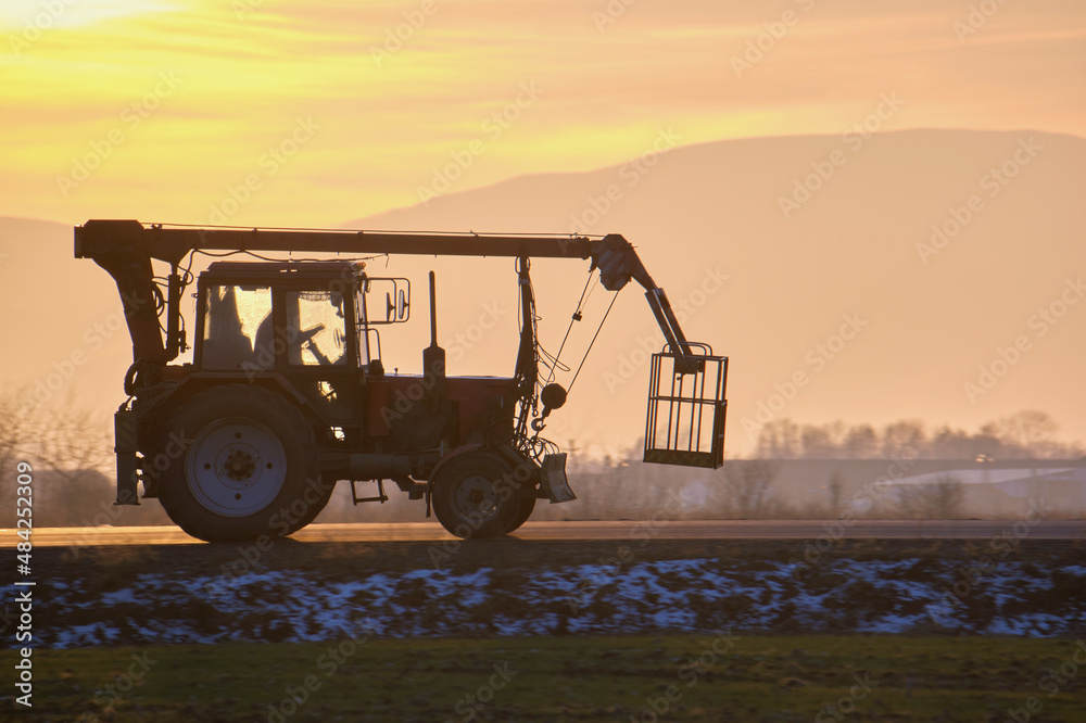 Fototapeta premium Mobile lifting crane tractor driving on intercity road at sunset