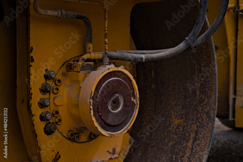 Oś wielkiego, wibracyjnego walca drogowego w kolorze żółtym . Yellow large vibrating road roller axle.