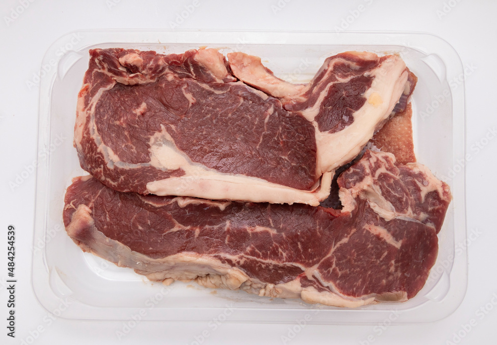 Two finger-thick ribeyes, tucked into a clear plastic tray. Isolated on white background. Isolated products concept.