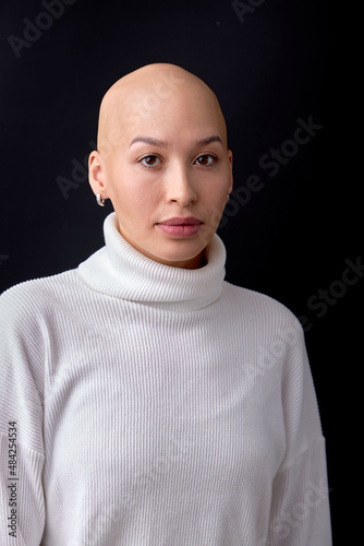 Fotografie Portrait of hairless female in white casual shirt looking at camera confidently, isolated over black studio background