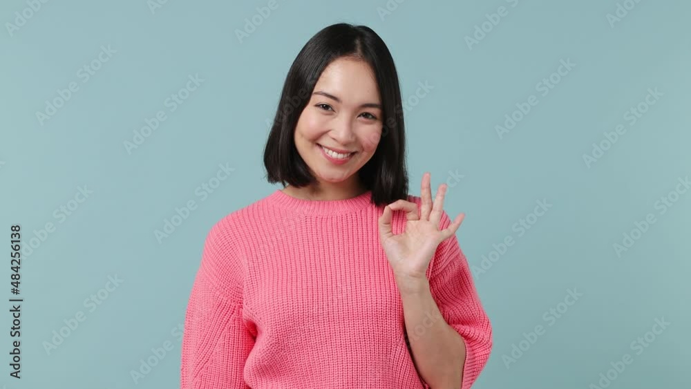 Vivid cheerful young woman of Asian ethnicity 20s wears pink shirt show okay ok zero fingers gesture isolated on plain pastel light blue background studio portrait. People emotions lifestyle concept