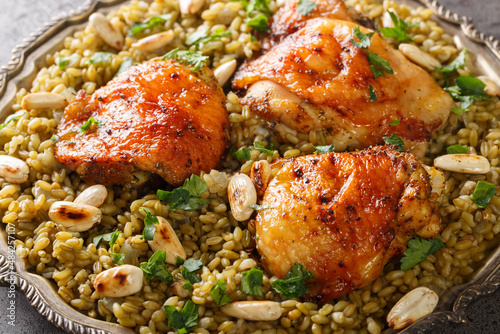 Lebanese chicken served on a bed of freekeh fire-dried green wheat with a garnish of toasted nuts closeup on the table. Horizontal photo