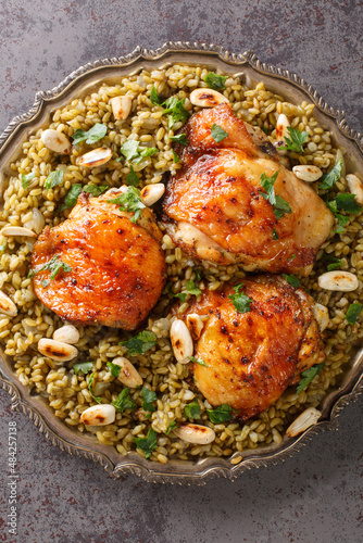 Freekeh with chicken is a delicious meal made with the grain and served with toasted nuts and herbs closeup in the plate on the table. Vertical top view from above photo