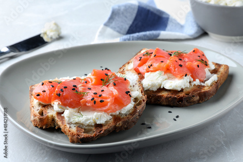 Fototapeta Naklejka Na Ścianę i Meble -  Delicious sandwiches with cream cheese, salmon and black sesame seeds on light grey table, closeup