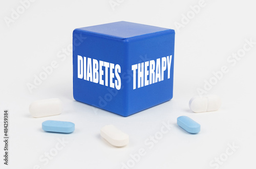 On a white surface are pills and a blue cube that says - DIABETES THERAPY