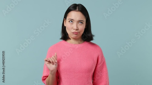 Frowning distempered preoccupied nervous young woman of Asian ethnicity 20s years old wears pink shirt showing thumb down dislike gesture isolated on plain pastel light blue background studio portrait photo