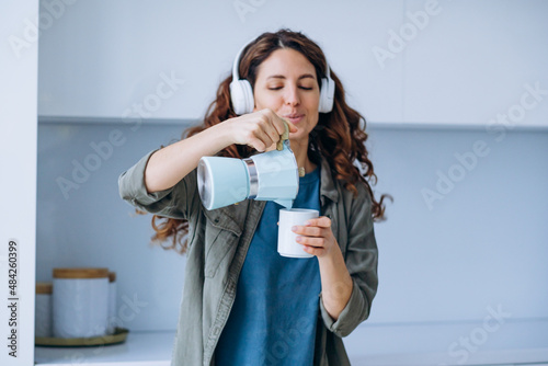 Bilde på lerret Curly-haired young woman with loose hairstyle dances to loud music in wireless h