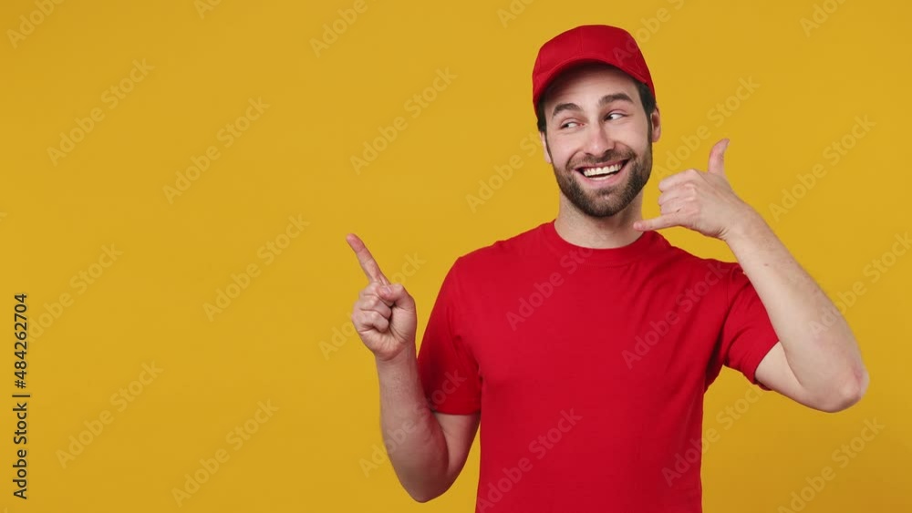 Professional delivery employee man in red cap T-shirt uniform workwear work as dealer courier point aside do phone gesture like says call me back isolated on plain yellow background studio portrait Professional delivery employee man in red cap T-shirt uniform workwear work as dealer courier point aside do phone gesture like says call me back isolated on plain yellow background studio portrait