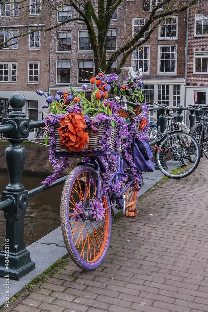 Bicycle decorated with colorful flowers parked on the canal bridge. Amsterdam, the Netherlands. 