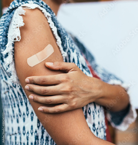 Arm of unrecognizable latin woman who just received a dose of coronavirus vaccine and holds the band-aid. Copy Space. Prevention.