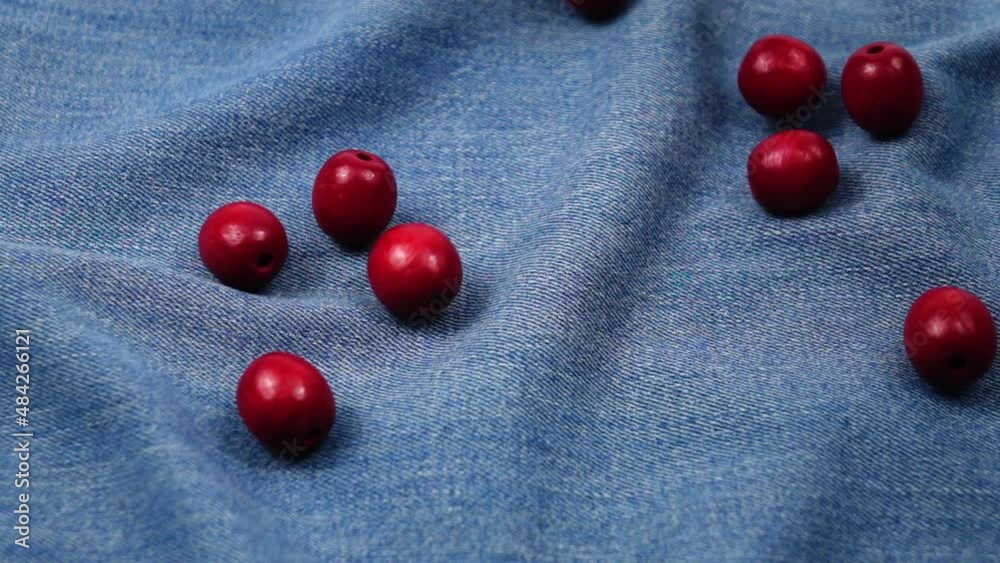 Big wooden red beads fall on the blue denim, background, slow motion Big wooden red beads fall on the blue denim, background, slow motion