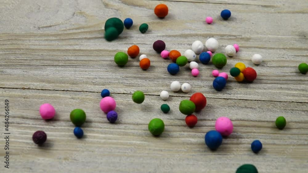 Multi colored plasticine balls fall and roll on the gray wooden board, slow motion. 