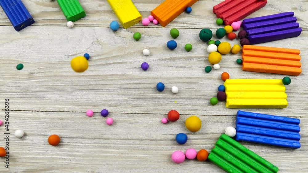 Multi colored plasticine balls roll on the gray wooden board with pieces of plasticine lying on it, slow motion. 