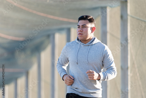 Latin runner jogging and wearing a hoodie