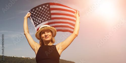 Young woman in a hat with an American flag on a sunset sky background. Portrait of a woman on the holiday of Independence Day 4th of July. USA symbol. Day off for AMERICA