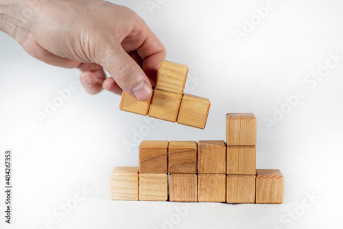 Creative forming figure from wooden cube blocks with human hand placing last piece of wood on white background