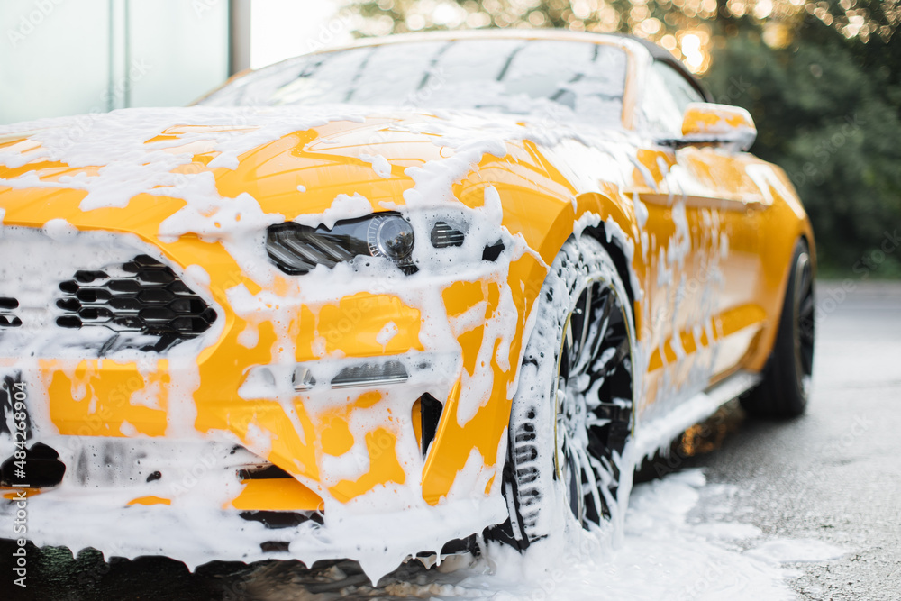 Cropped image of wheel of luxury yellow car in outdoors self-service car wash, covered with cleaning soap foam. - obrazy, fototapety, plakaty 