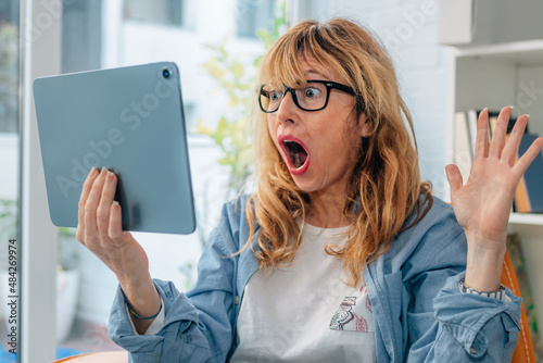 astonished or surprised woman looking at computer or tablet at home photo