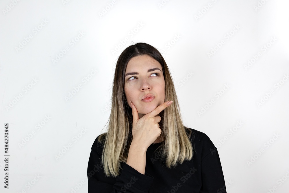 Young beautiful girl wearing casual clothes over isolated white background with hand on chin thinking about question, pensive expression. Smiling with thoughtful face. Doubt concept. Young beautiful girl wearing casual clothes over isolated white background with hand on chin thinking about question, pensive expression. Smiling with thoughtful face. Doubt concept.