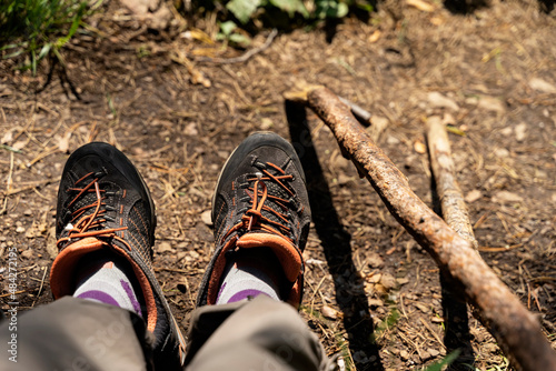 Legs in tracking sneakers and wooden hiking poles. Active and healthy lifestyle in summer