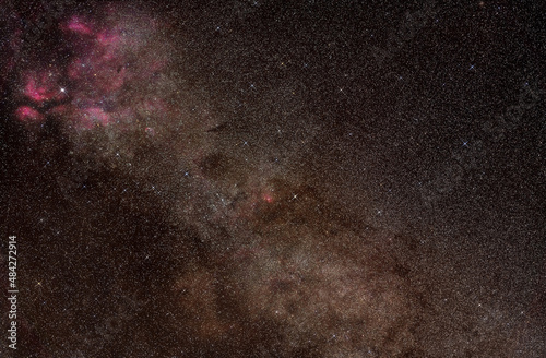 Night sky, many stars with milky way around Cygnus constellation, Red purple nebulosity around Sadr star visible. Long exposure stacked photo