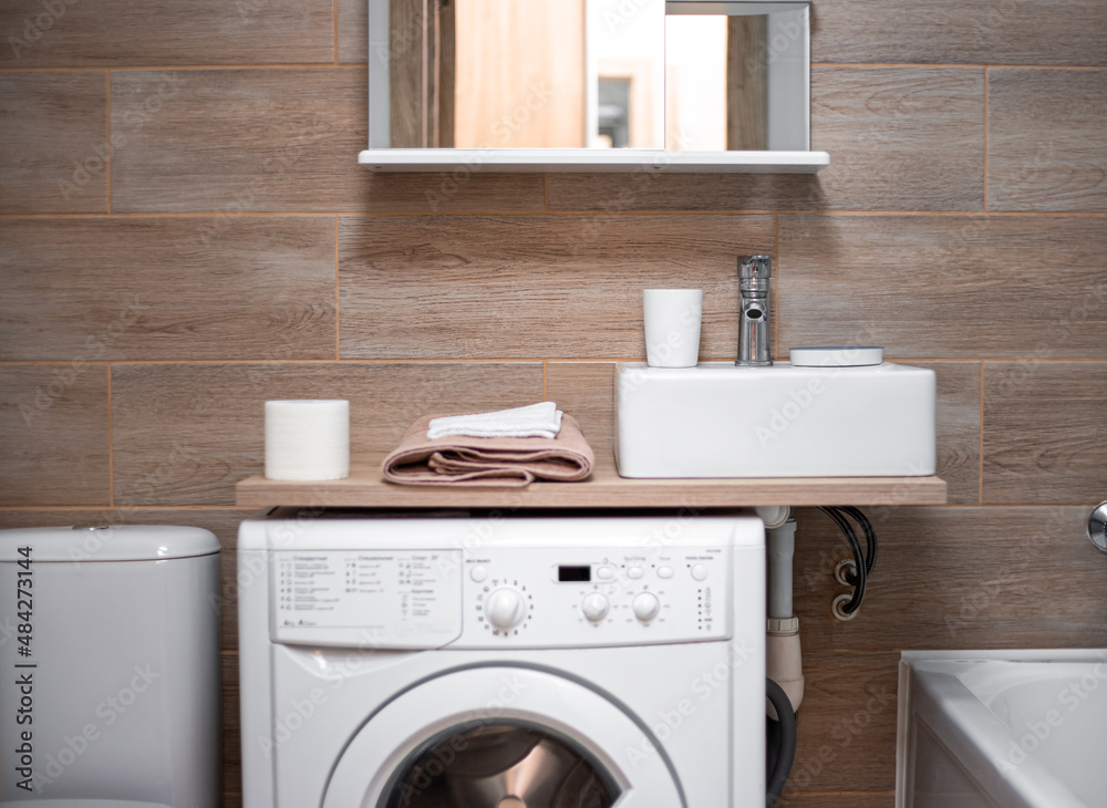 Bathroom interior. Compact placement of the sink, shelf, washing machine and toilet bowl Bathroom interior. Compact placement of the sink, shelf, washing machine and toilet bowl