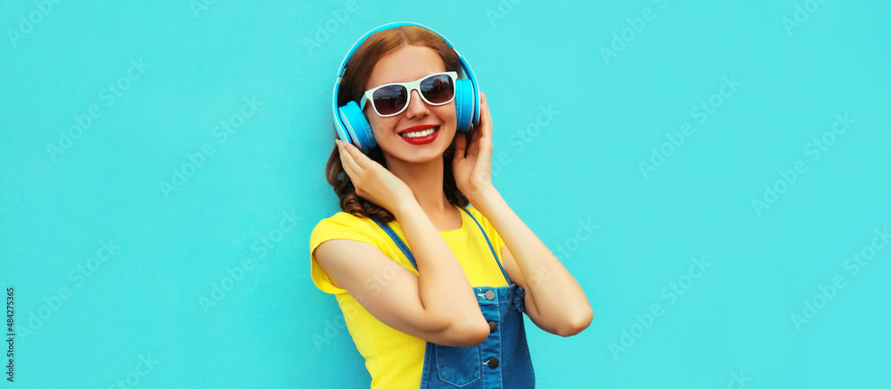 Portrait of happy smiling woman listening to music in headphones on colorful blue background