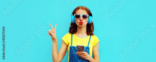 Portrait of young woman in headphones listening to music with phone on blue background photo
