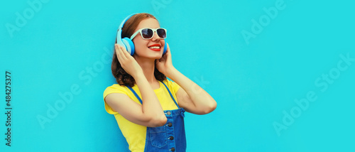 Portrait of happy smiling woman listening to music in headphones on colorful blue background