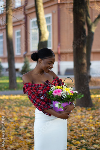 Side view of two beautiful African women in a park holding bouquets of flowers.