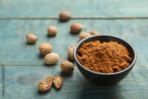 Bowl of nutmeg powder and seeds on light blue wooden table