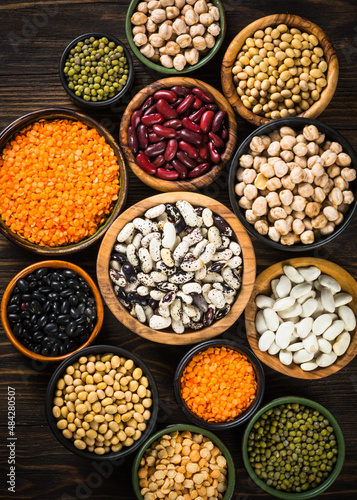 Legumes, lentils, chikpea and beans assortment in different bowls on wooden table. Vegan food, alt meat.