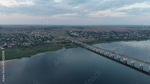 Flying near automobile bridge with car over the river. There is a city on one bank of the river