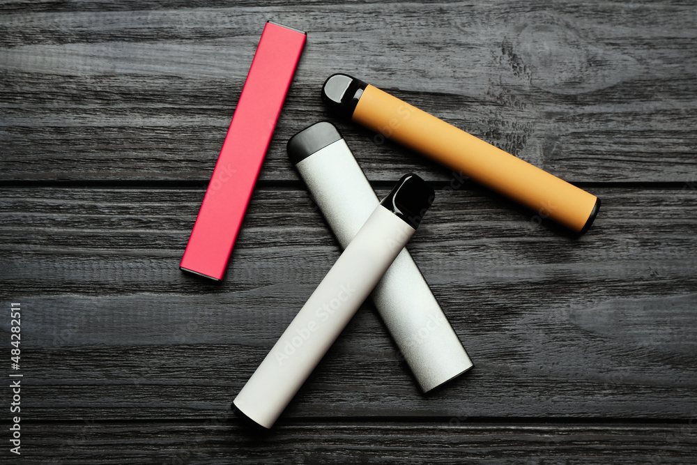 Different disposable electronic cigarettes on black wooden table, flat lay. Smoking alternative Different disposable electronic cigarettes on black wooden table, flat lay. Smoking alternative