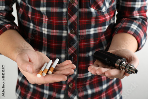 Man with cigarettes and vaping device on light background, closeup. Smoking alternative