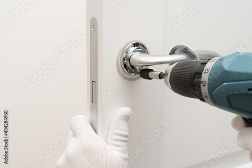 Screwdriver in the hands of a service man installing lock and door handle on interior door.