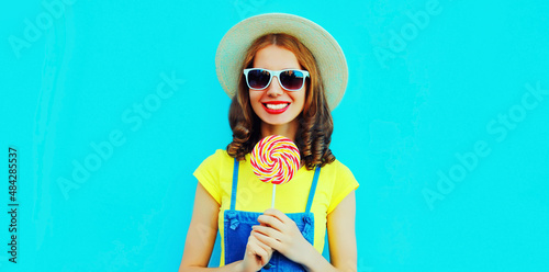 Summer portrait of happy smiling young woman with lollipop wearing straw hat on blue background